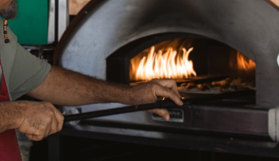Détail des mains d'un pizzaiolo maniant la pelle devant les flammes du four