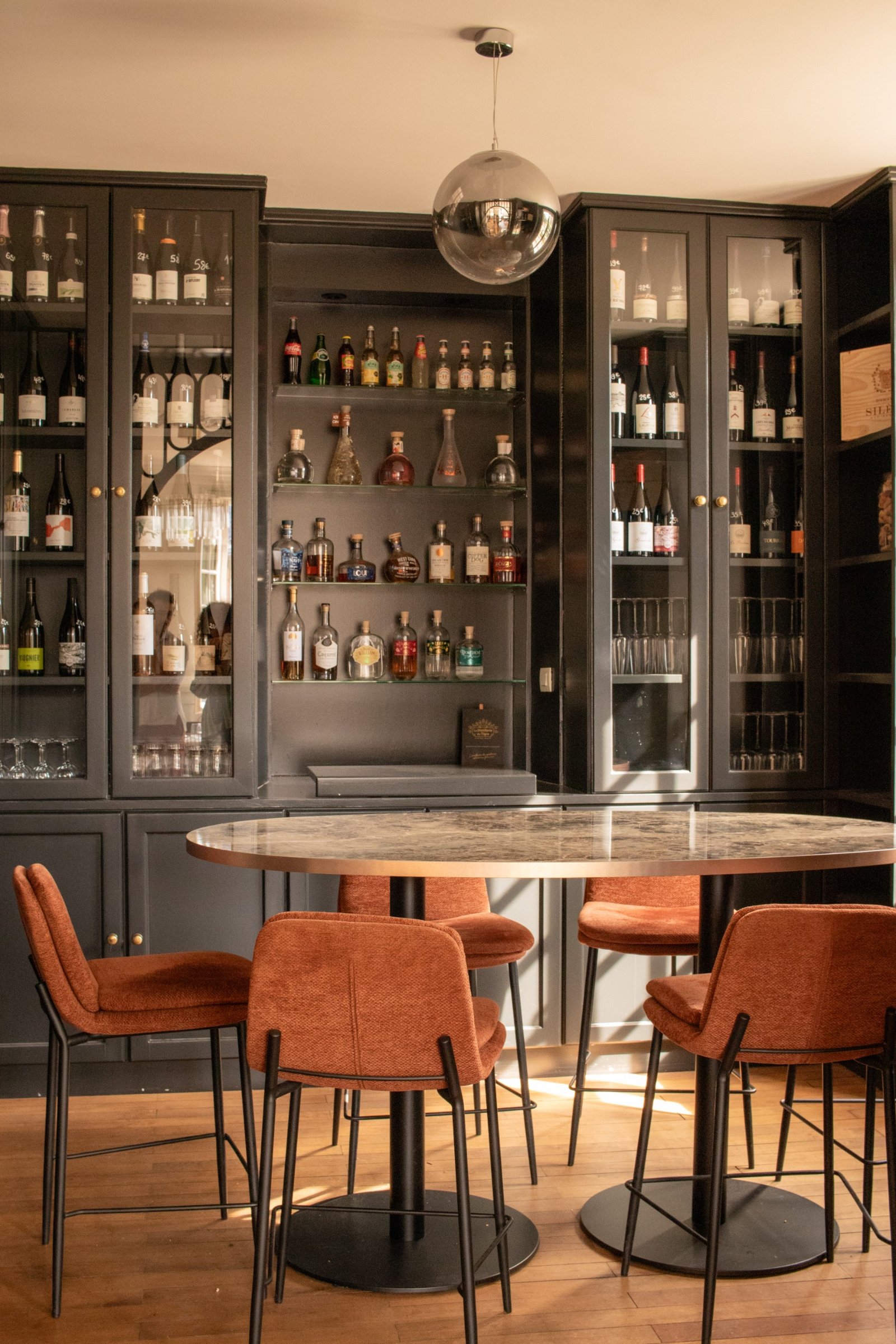 Bar sombre garni de bouteilles avec fauteuils rouille et lumière naturelle chaude