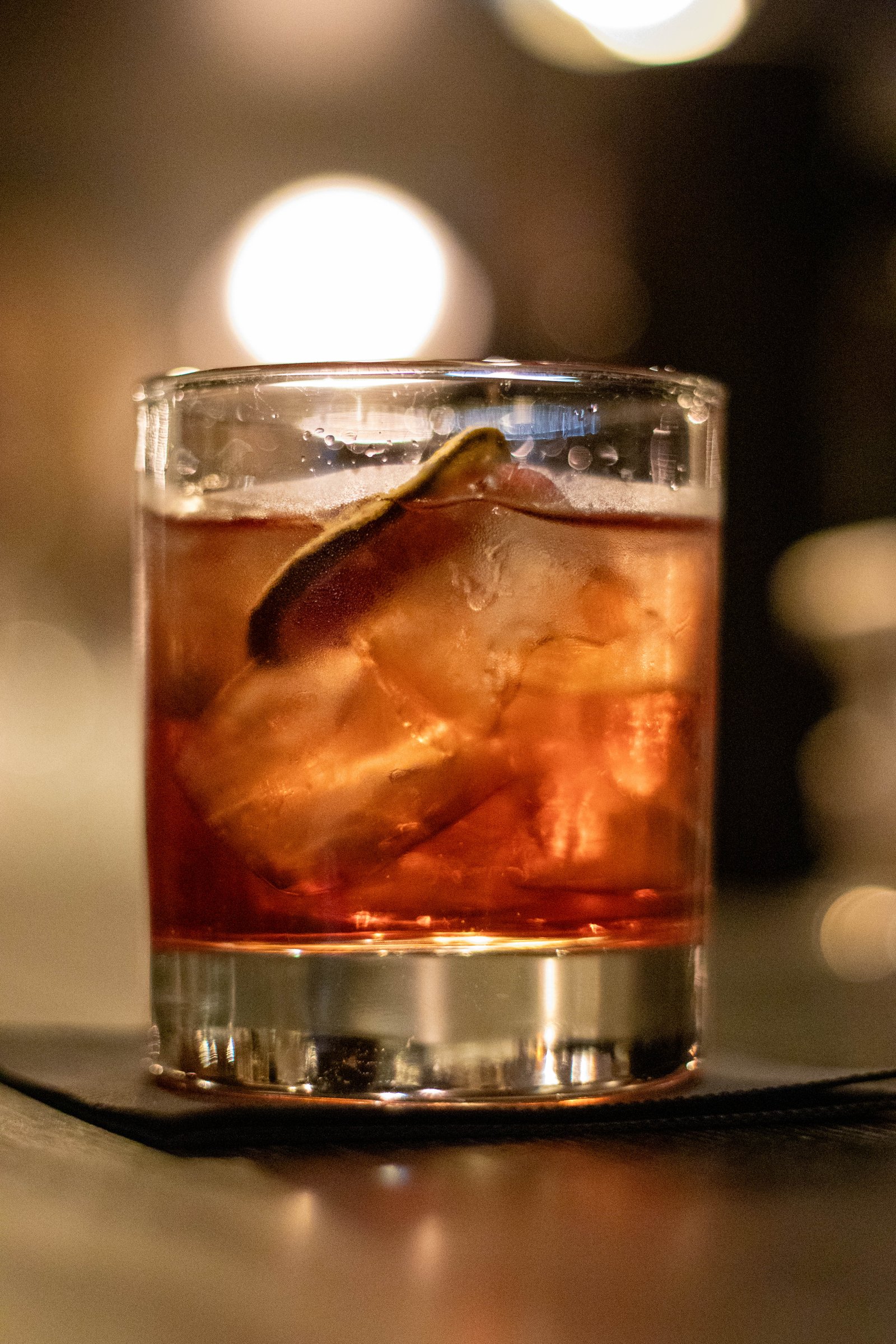 Cocktail ambré sur glace, éclairé en contre-jour dans une ambiance de bar tamisée